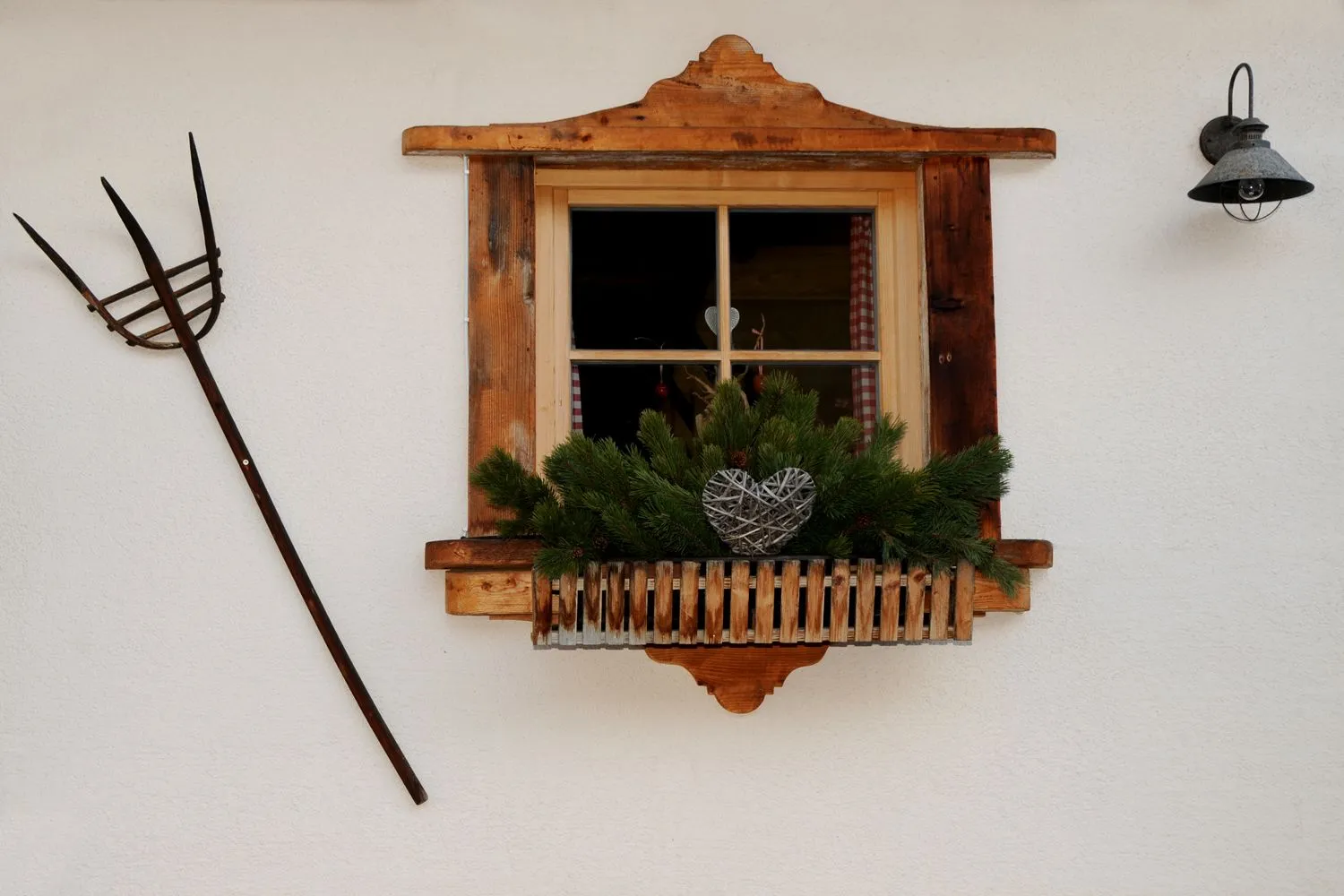 Sprossenfenster mit Blumenkasten und alter Heugabel an der Hauswand