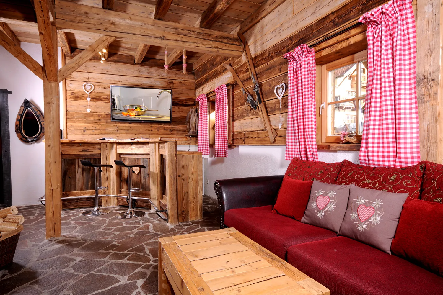 Wohnbereich mit rotem Sofa, Holzsäulen und Bar im Almchalet am Hochkönig